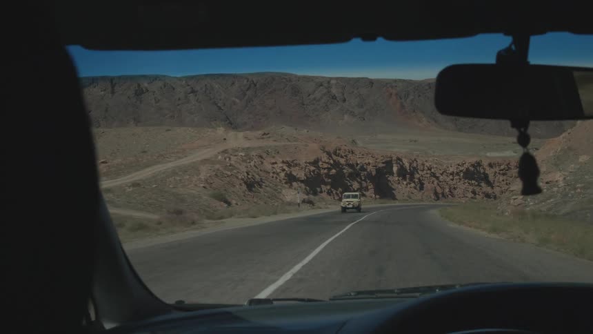 View of the inner windshield of a vehicle moving along a twoway road in a natural environment with rocky mountains around