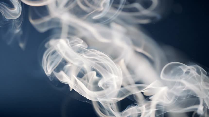 Extreme closeup of whitish smoke rising in slow motion on a dark blue background