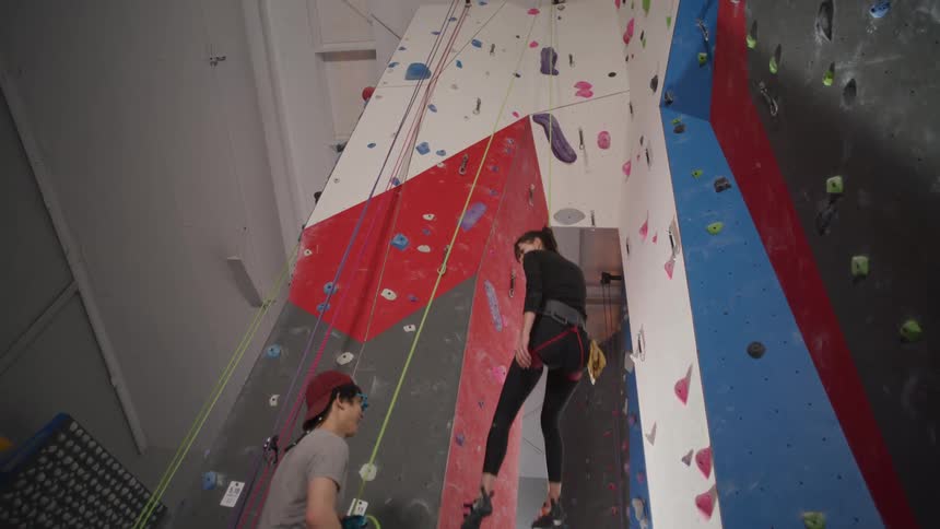 Woman wearing a safety harness descending a training climbing wall and clapping hands with her colleague