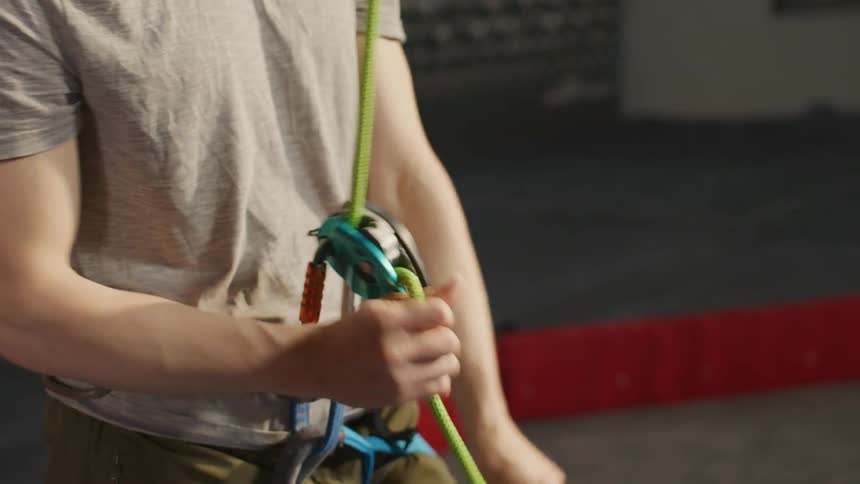 Arms of a man pulling a rope that is attached to the climbing harness at his waist