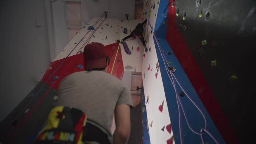 Man providing support as belayer to his colleague who is climbing an indoor climbing wall