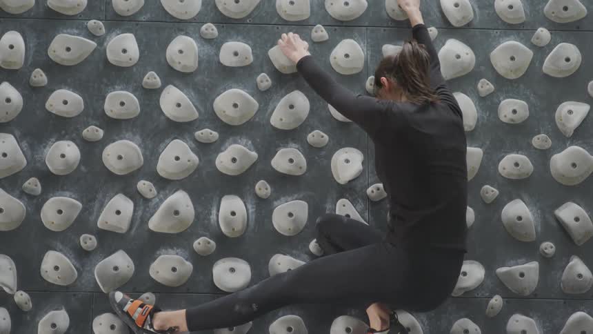 A climber is reaching for the next hold on a kilter board wall