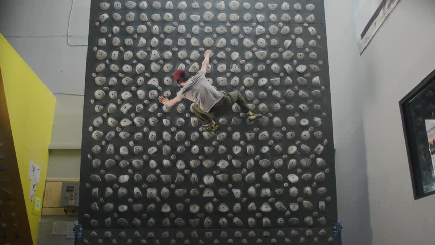 A young man trains on a kilter board climbing wall with a variety of hold types