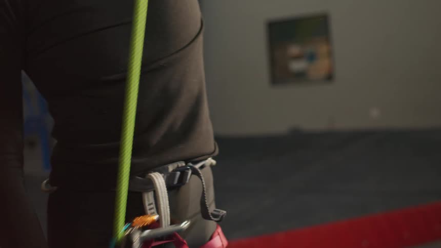 View of a womans waist tightening a rope on her climbing harness
