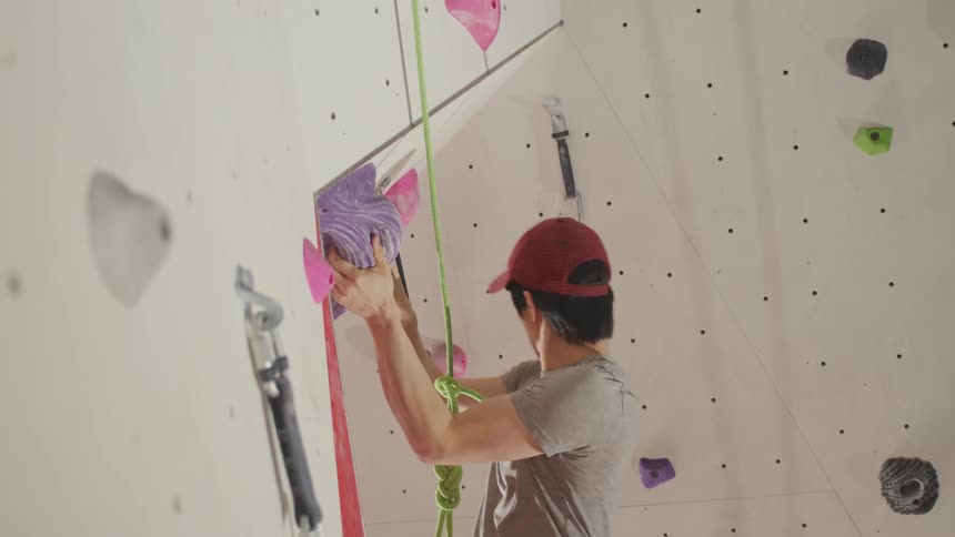 Asian man rock climbing indoors on a rock climbing wall at a gym