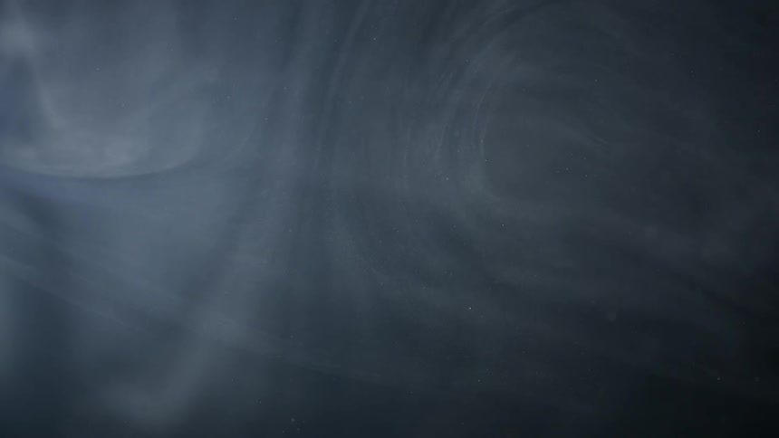 Whisps of smoke and small particles floating against a dark background