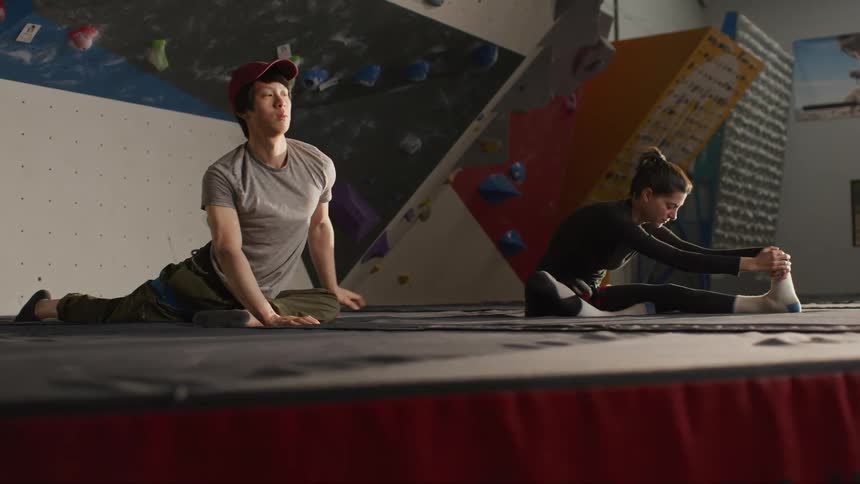 A young man and woman are sitting on the floor and stretching