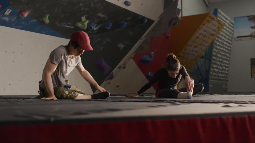A young man and woman are stretching while sitting on a large mat