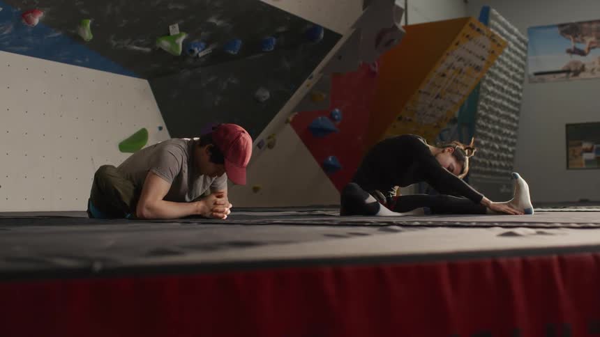 Man and woman sitting indoors stretching their legs and body