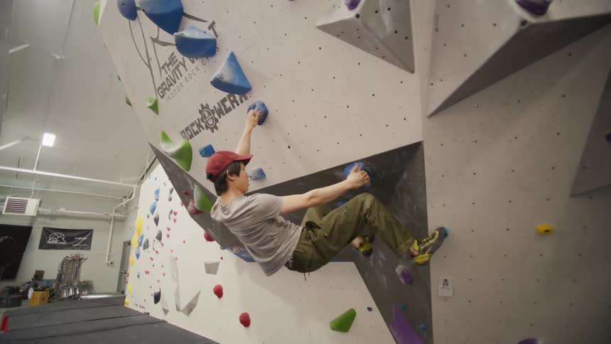 Male rock climber grips hold points while climbing wall in a climbing gym