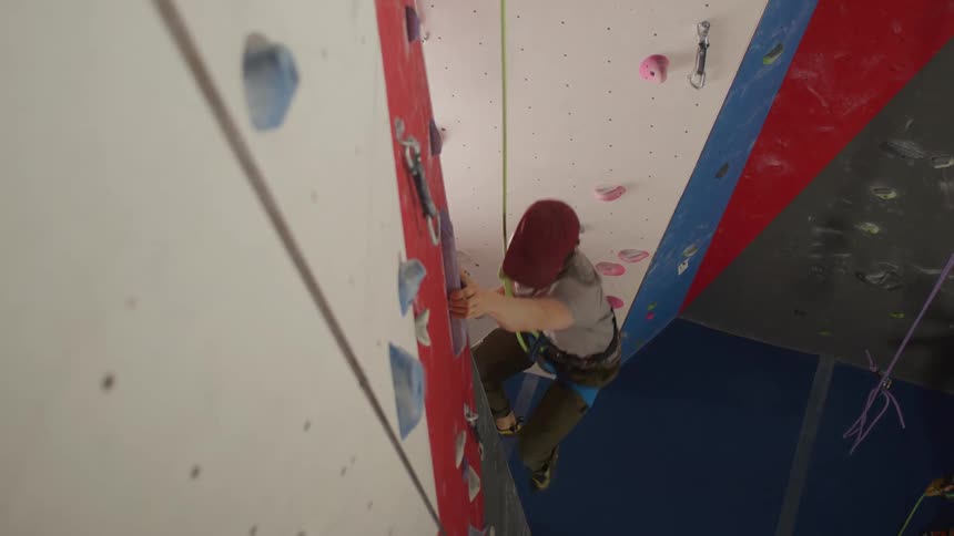 A man is climbing up the rock wall in the gym