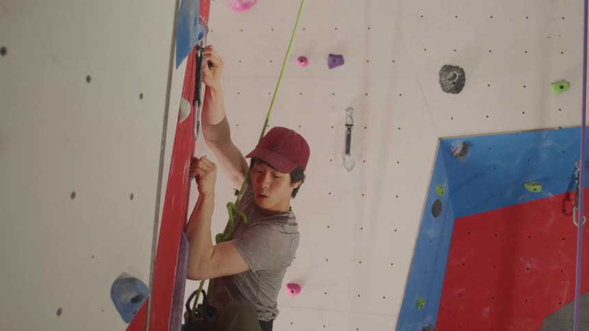 Young asian man training on a fake climbing wall with a safety rope