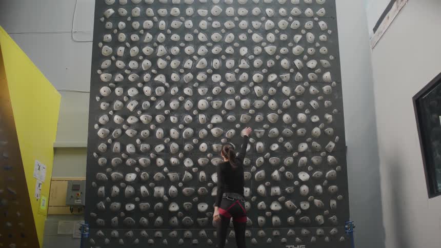 A tall athletic woman begins to ascend an indoor climbing wall