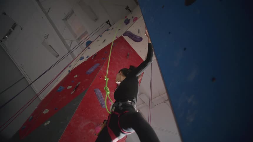 Woman with harness rope climbing a mountain simulation wall