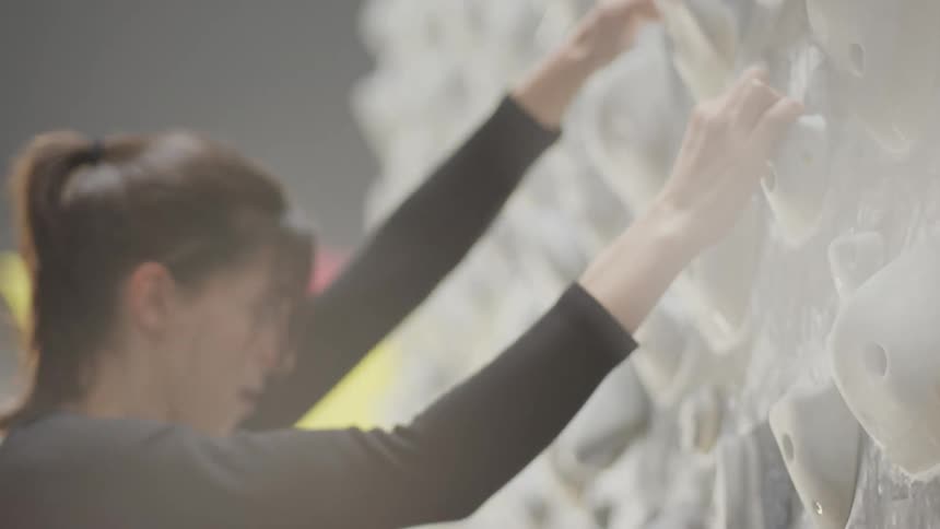A young woman climbs a kilter board wall in a climbing gym