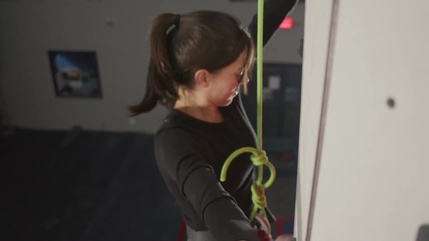 A woman uses a rope to climb in a climbing gym