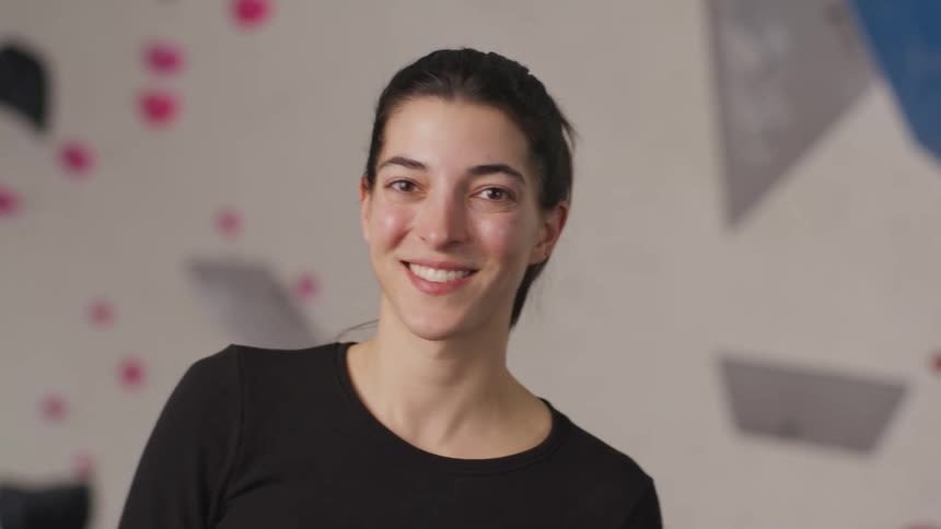 A woman wearing a black shirt looks to the side and then straight ahead and smiles