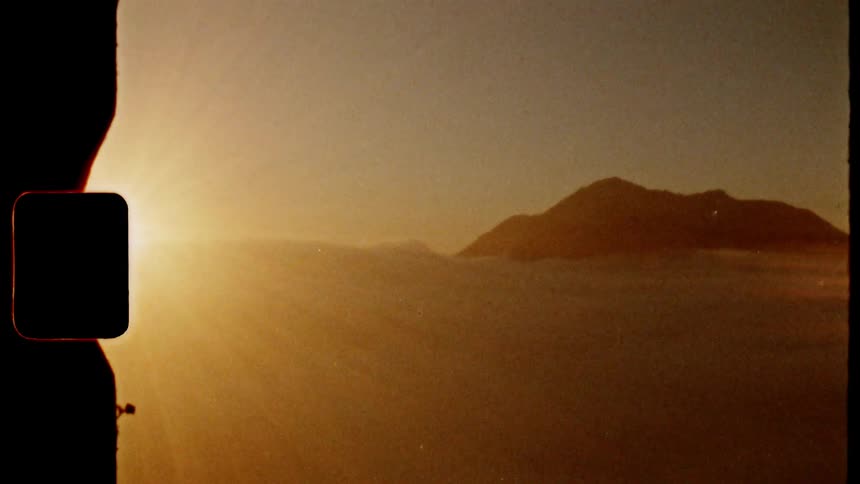 The view from the top of a mountain where you can see the top of another mountain amidst clouds and strong rays of sunlight