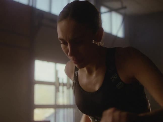 Woman sweats while pedaling on exercise machine in a gym with a high ceiling
