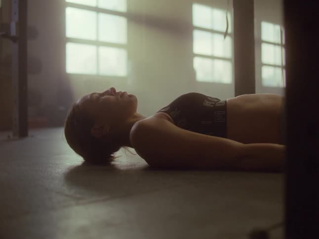 Woman lies down on floor of gym breathing hard after exercising