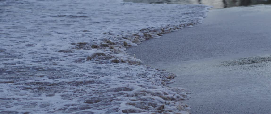 Several ocean waves wash upon a sandy beach coastline