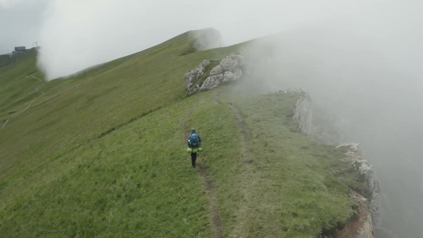 Person hiking on a mountain next to a cliff on a foggy day