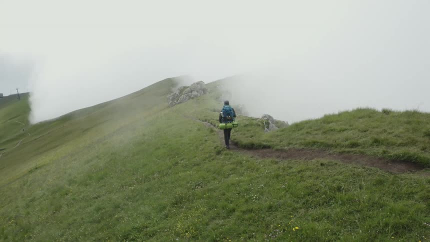 Backpacker hikes along path near cliff overlooking a foggy valley