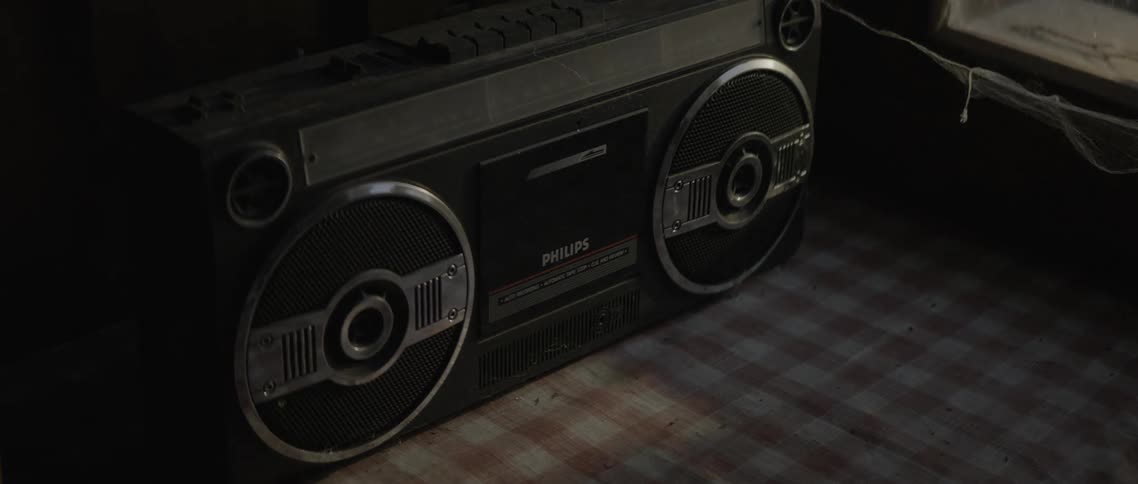 A black boombox sits on a checkered tablecloth in a dark room