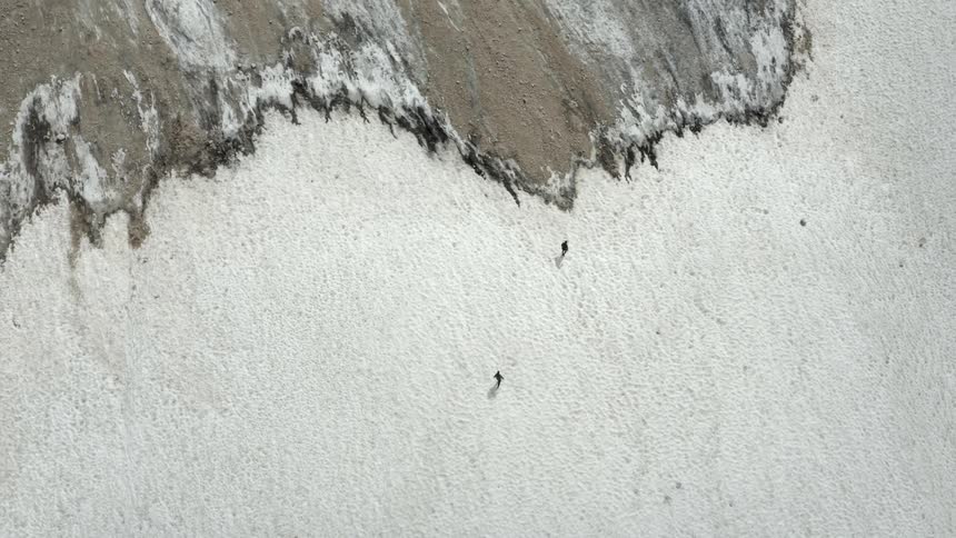 Aerial panorama of two people hiking on rocky snowy ground