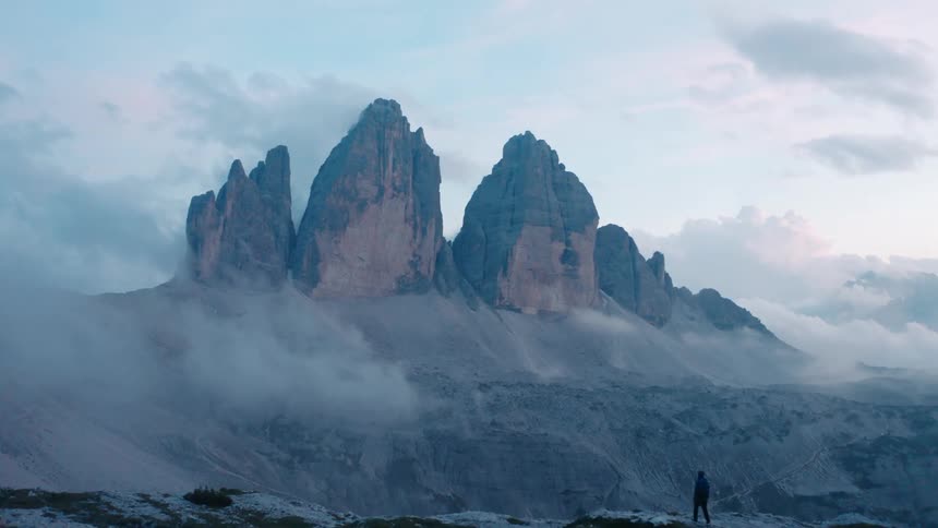 Landscape of a man walking on a cliff overlooking three rocks on a mountain peak in the morning