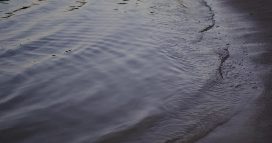 Close up of the tide gently rolling onto a black sandy shoreline at dawn