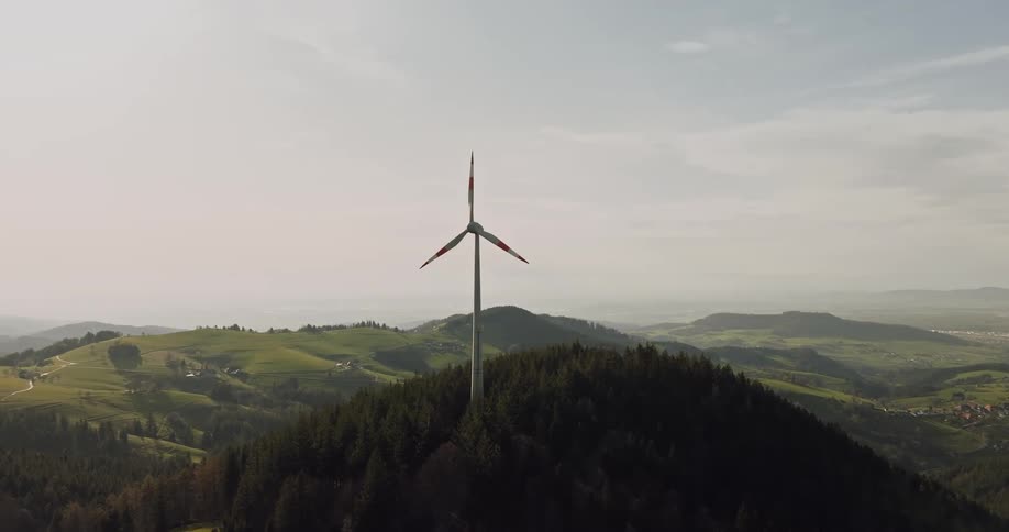 Aerial panorama of a wind power tower on a mountain with a city on the horizon