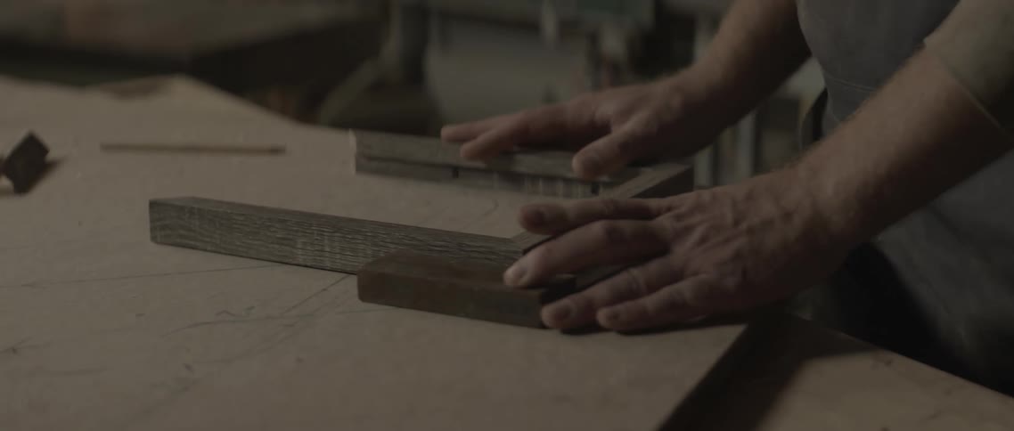A man aligns a few pieces of wood frames together on a workbench