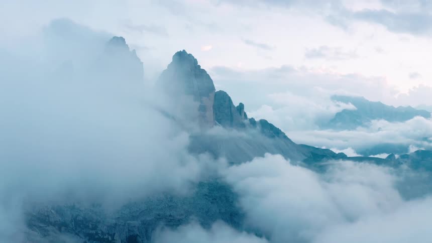 Mountain peaks stand high above clouds moving over mountains