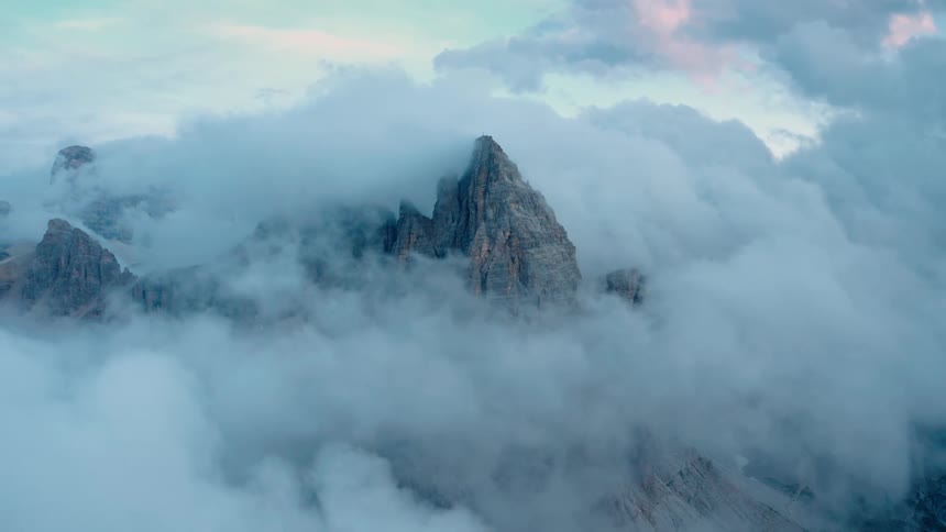 The aerial view of the rocky mountain peak covered by clouds