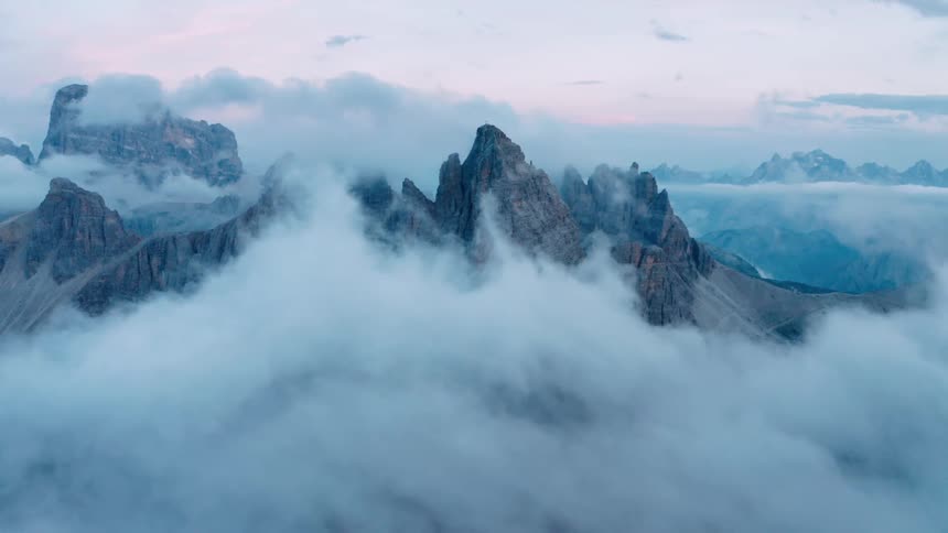 Mountain peaks stand high above clouds moving over mountains