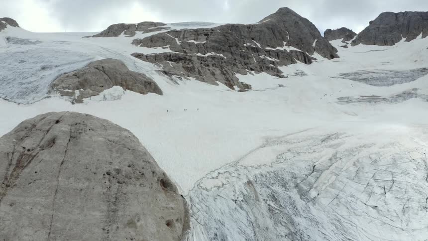 Four people walking across a glacier in a mountain valley