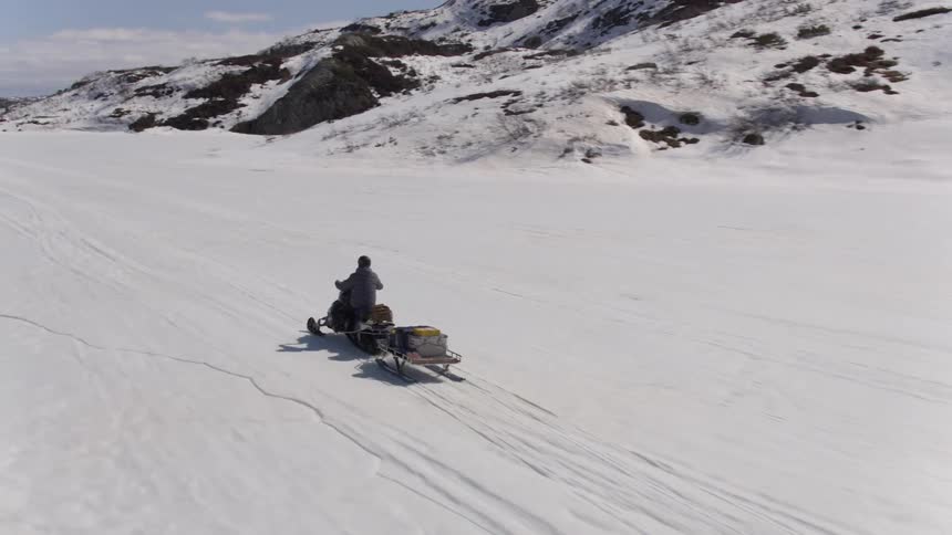 A person riding a snow mobile with a trailer behind it