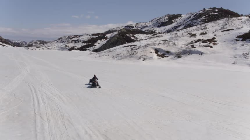 A person drives up a snowy mountain slope on a snowmobile