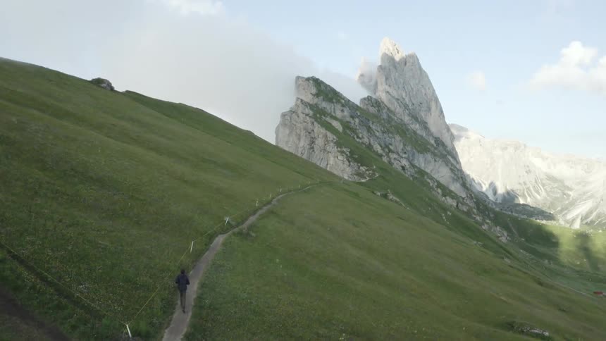 A person runs along a trail near the top of a mountain range on a summer day