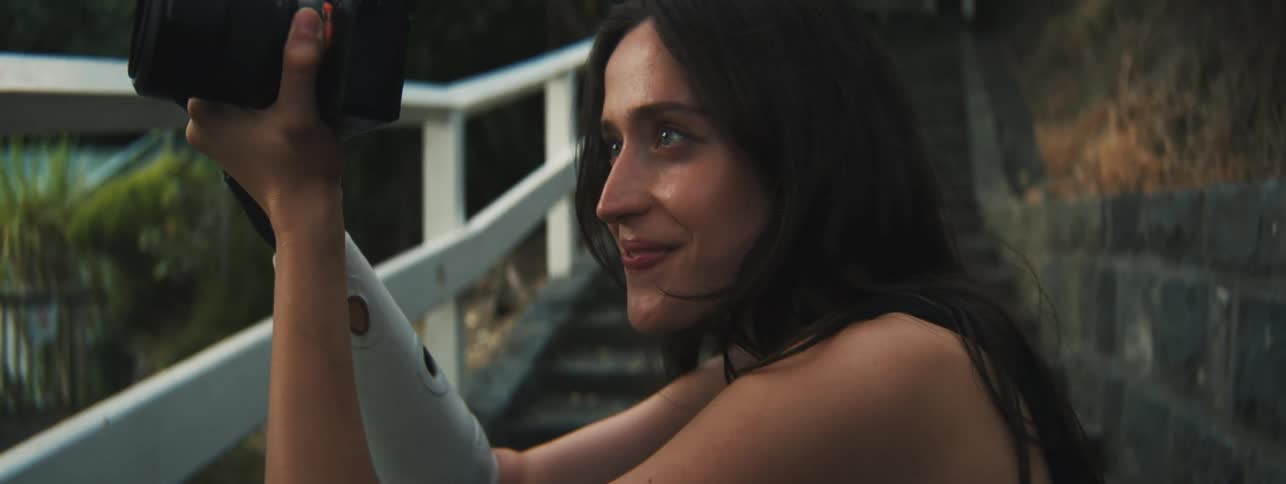Woman crouching down giving a slight smile while using her professional camera in an outdoor environment