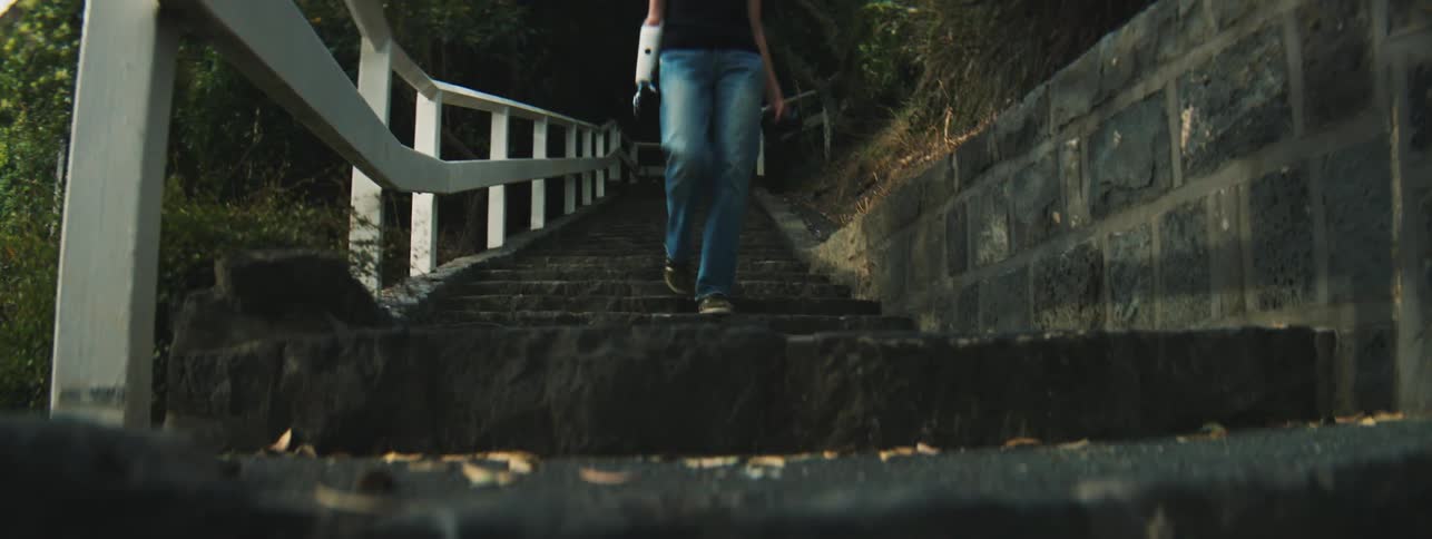 Legs of a woman walking down the stairs in an outdoor environment holding a professional camera in one of her hands
