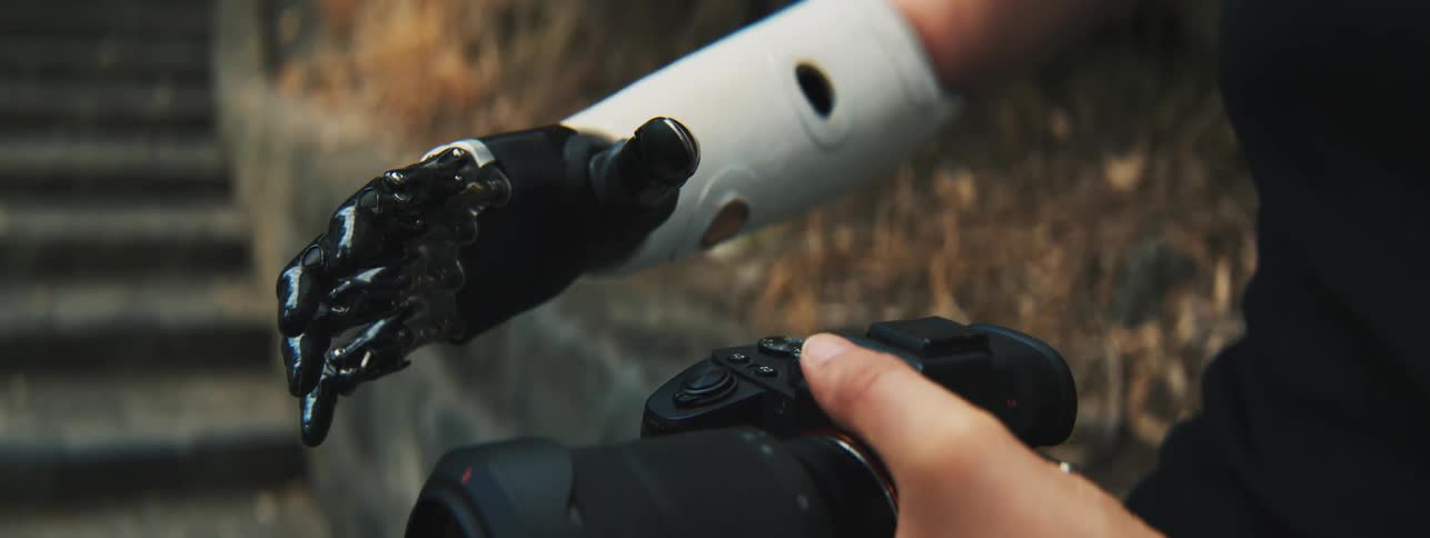 Closeup of a womans hands one of which is robotic and holding a professional camera