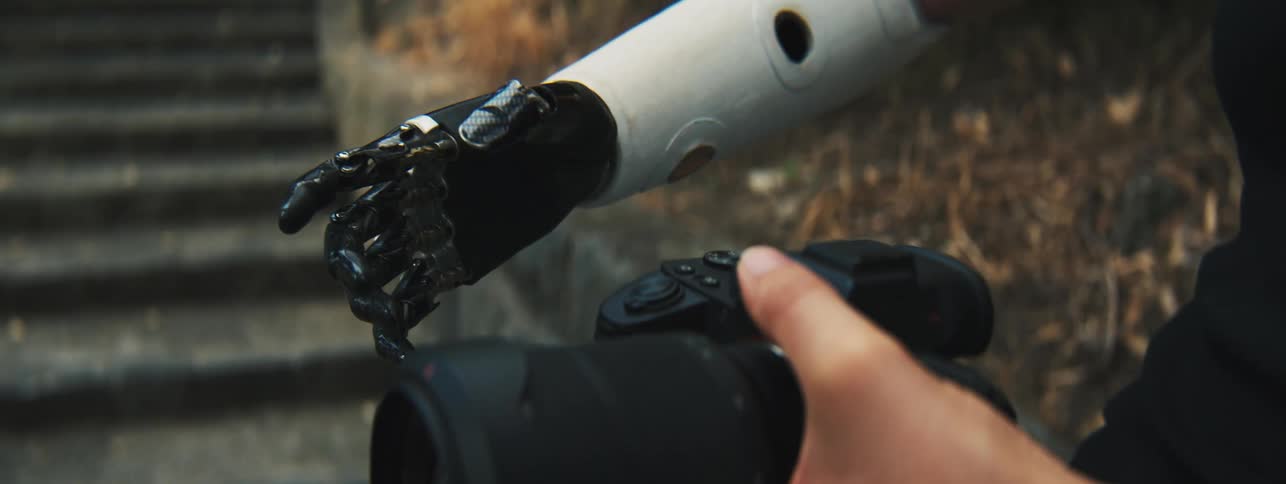 Lady with a robotic arm holds a camera on the other hand while standing on the stairs outdoor