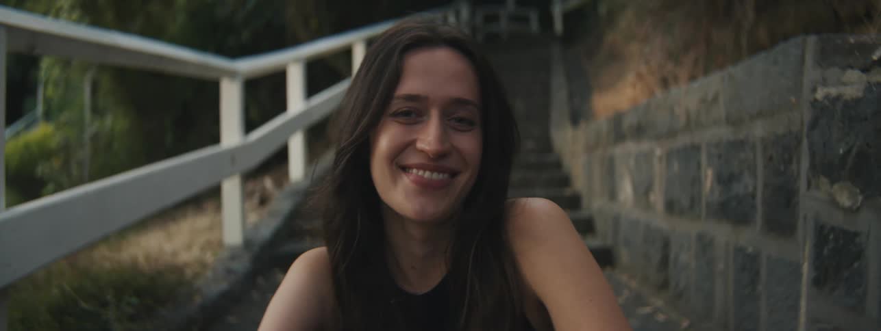 A woman smiling as shes sitting in a stone path with a wooden guard rail