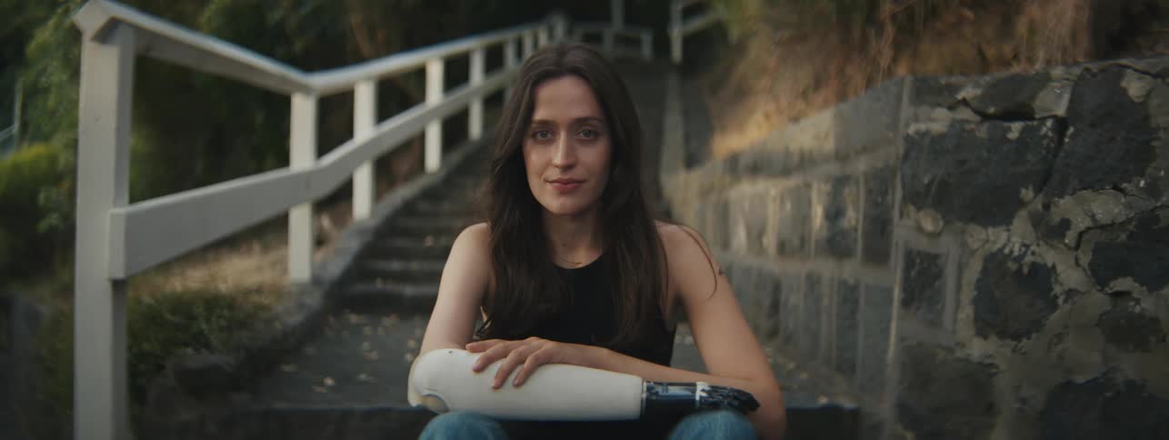 Young woman sitting on the stairs in an outdoor environment with vegetation and one of her arms is mechanical