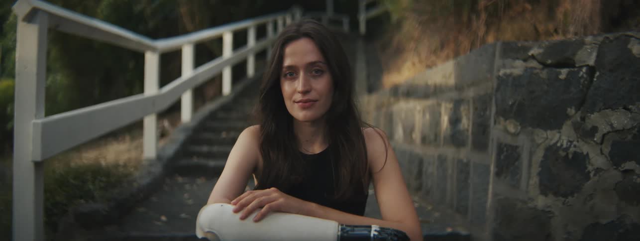 Young woman sitting on the steps of a neighborhood with one of her mechanical arms