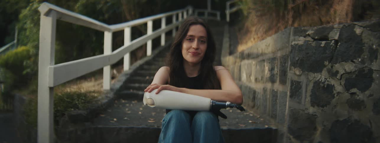 A female smiling while seated on the stairs outdoor with a robotic arm