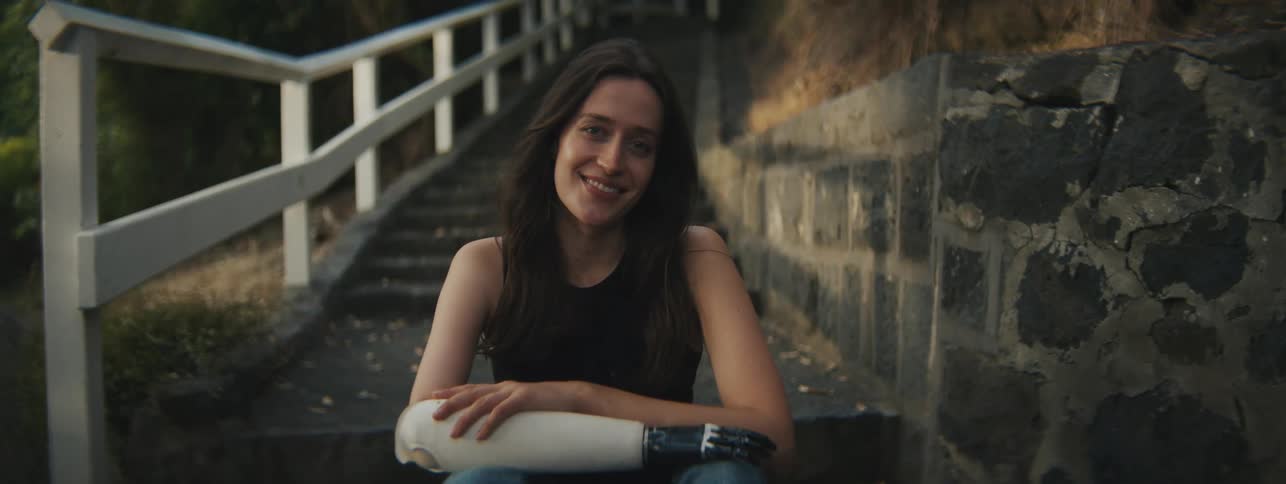 A woman sits on a staircase next to a white railing and a stone wall