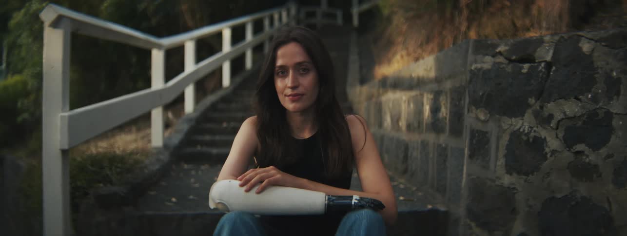 A woman with an artificial arm sits outdoors